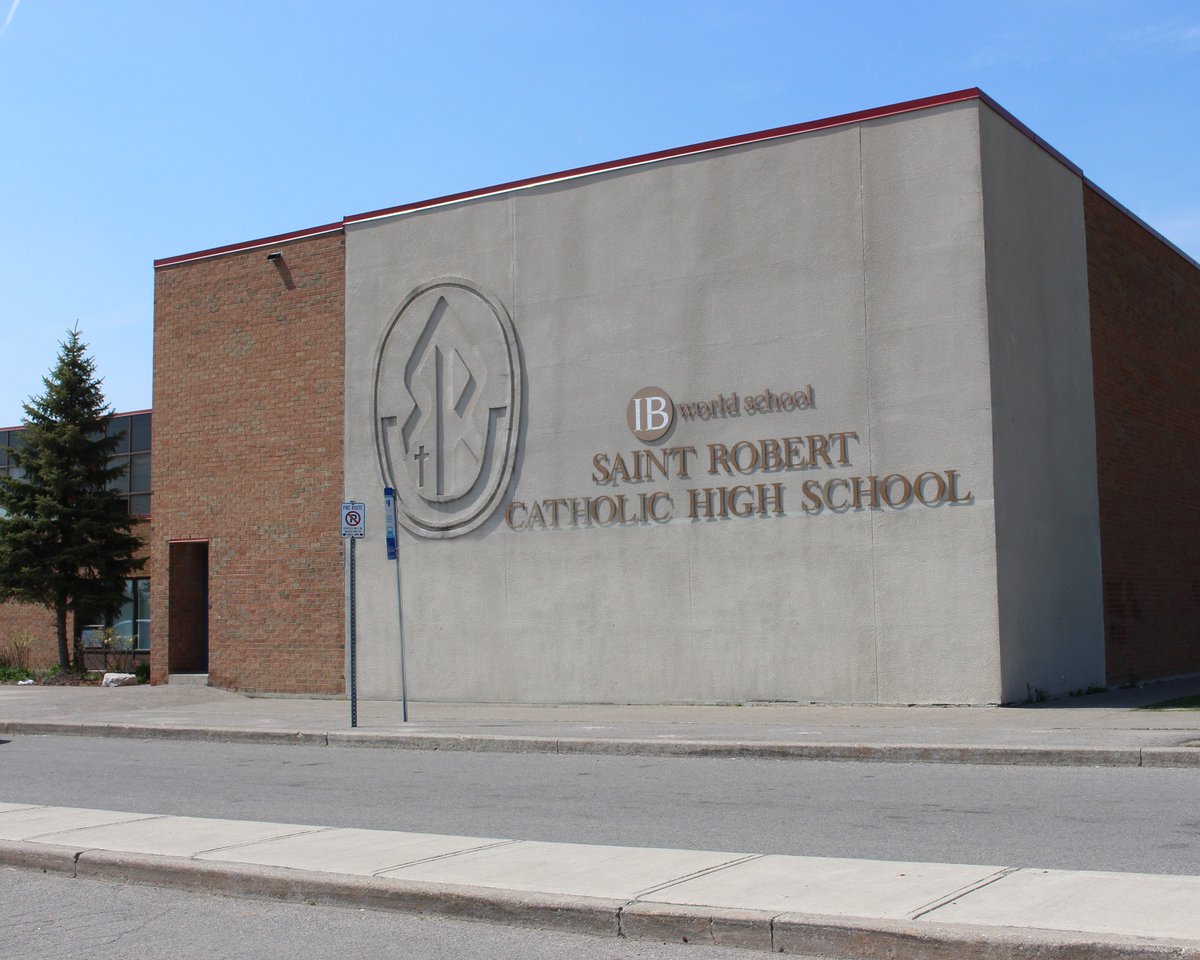 A picture showing the front-side of St. Robert CHS. It is a brown building. Against a white outer wall, it reads: IB World School. Below that, it reads: Saint Robert Catholic School.