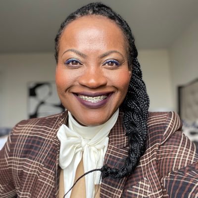 Image showing Miss Nadine Williams smiling. She is wearing a brown coat over a white shirt with a bow.